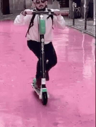 Man Riding Scooter Down Pink Street GIF