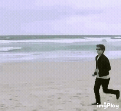 Man Running On Beach Next To Yellow Sign GIF
