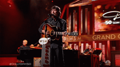 Man Singing Into Microphone Holding Guitar With WSM Sign GIF