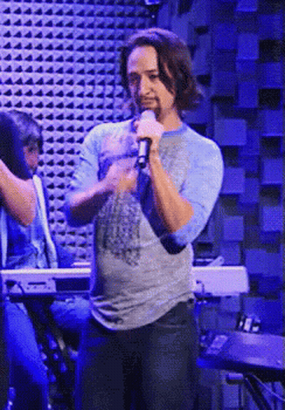 Man Singing Into Microphone In Front Of Blue Wall GIF