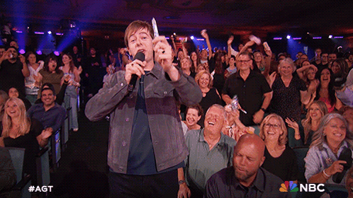 Man Singing Into Microphone In Front Of Crowd With NBC Logo GIF