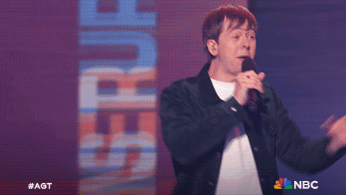 Man Singing Into Microphone In Front Of Saturn Sign GIF