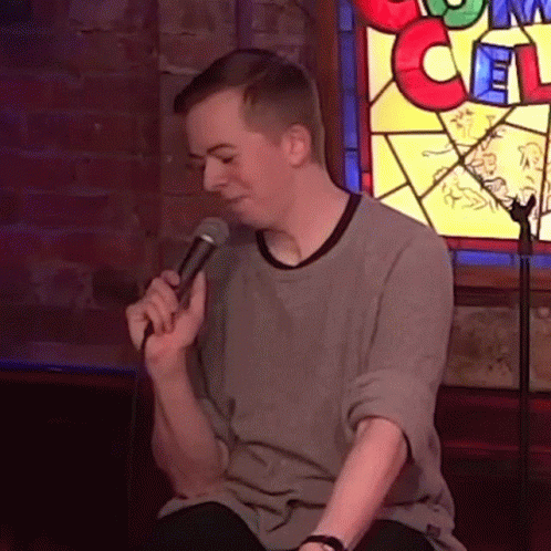 Man Singing Into Microphone In Front Of Stained Glass Window With Letter C GIF