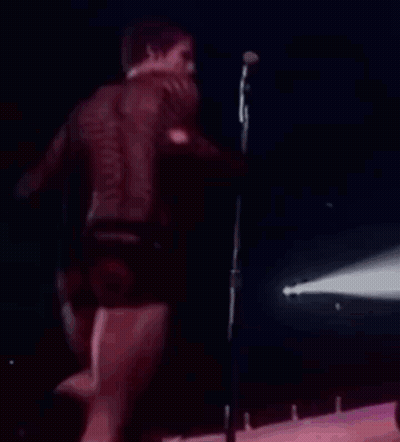Man Singing Into Microphone On Stage In Shorts GIF