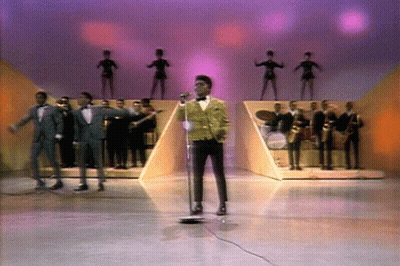 Man Singing Into Microphone On Stage With Band GIF