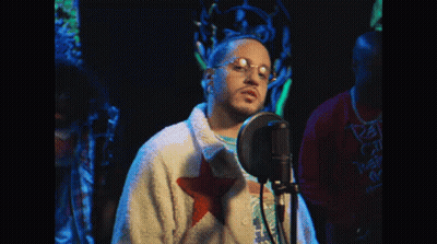 Man Singing Into Microphone With Glasses And White Jacket With Red Star GIF