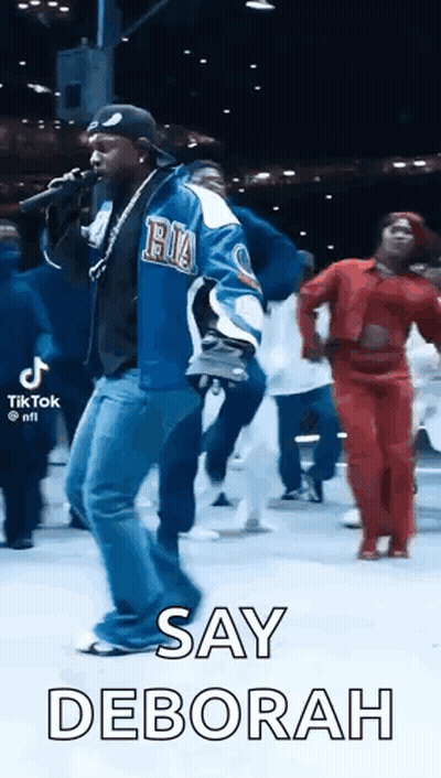 Man Singing Into Microphone With People Dancing Behind GIF