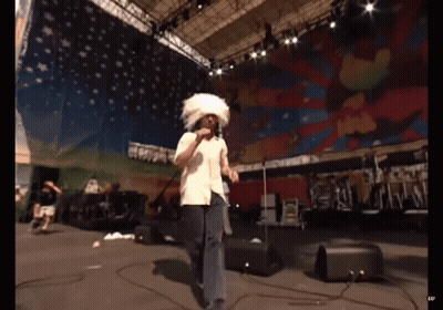 Man Singing Into Microphone With White Feathered Hat GIF