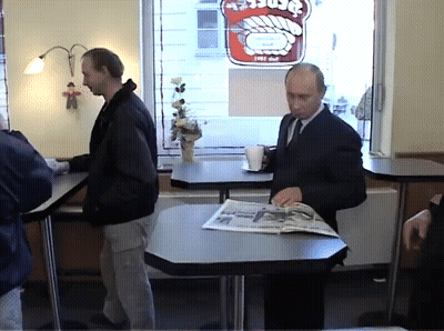 Man Sits At Table With Newspaper In Front Of Window With Burger Sign GIF