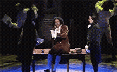 Man Sitting At Desk On Stage In Dark Room GIF