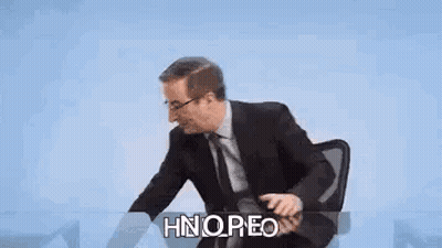 Man Sitting At Desk With Finger To Lips GIF