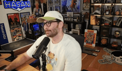 Man Sitting At Microphone With Sign Saying Hasan GIF