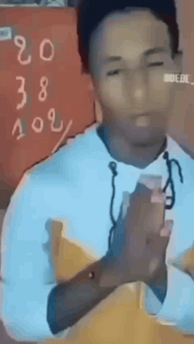Man Sitting At Table With Hands Folded In Front Of Chalkboard With Numbers GIF