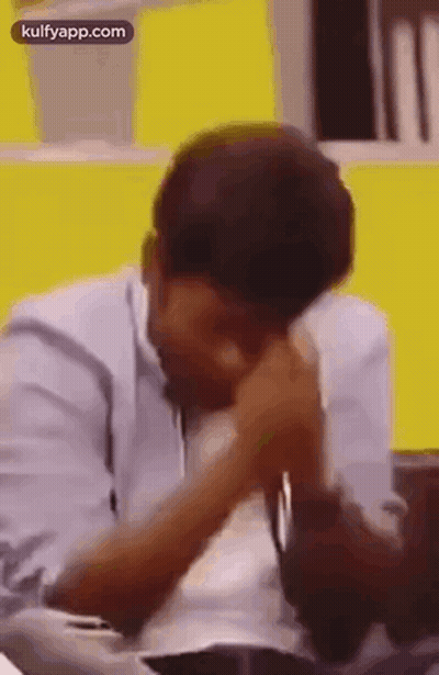 Man Sitting At Table With Hands On Face And Yellow Wall GIF