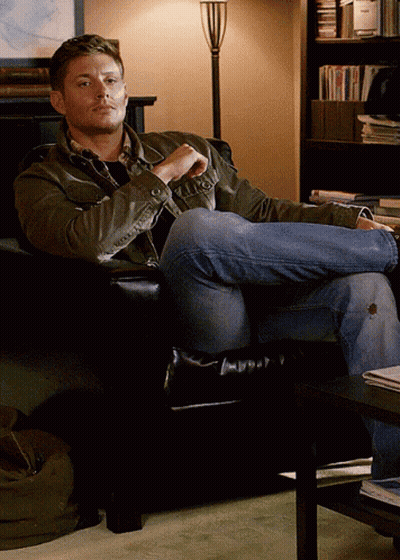 Man Sitting Cross-Legged In Chair Before Bookshelf GIF