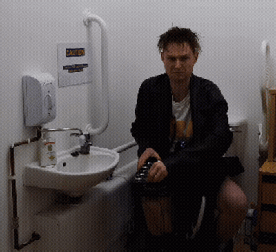 Man Sitting In Bathroom With Caution Sign GIF