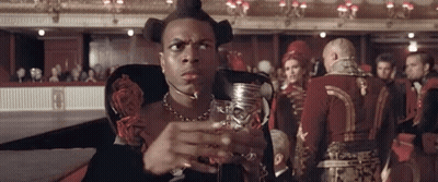 Man Sitting In Chair Holding Wine In Front Of Crowd GIF