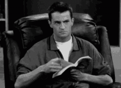 Man Sitting In Chair Reading Book Making Funny Face GIF