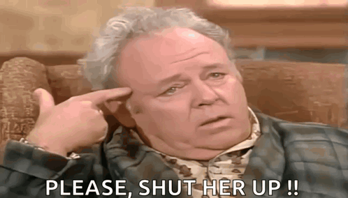 Man Sitting In Chair With Finger To Forehead Asking To Shut Her Up GIF