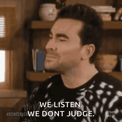 Man Sitting In Front Of Bookshelf Saying We Listen We Don't Judge GIF