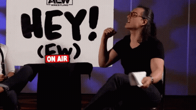 Man Sitting In Front Of Sign Saying Hey GIF