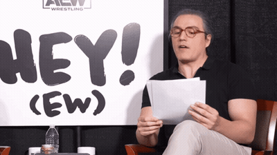 Man Sitting In Front Of Sign Saying Hey GIF