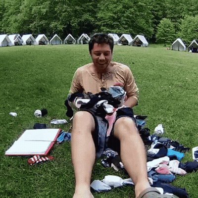 Man Sitting In Grass With Pile Of Clothes GIF