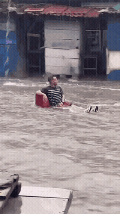 Hombre sentado en una hielera roja en una calle inundada GIF
