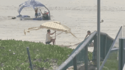 Man Sitting On Beach Holding Yellow And White Umbrella GIF