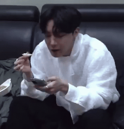 Man Sitting On Couch Eating And Looking At Phone GIF