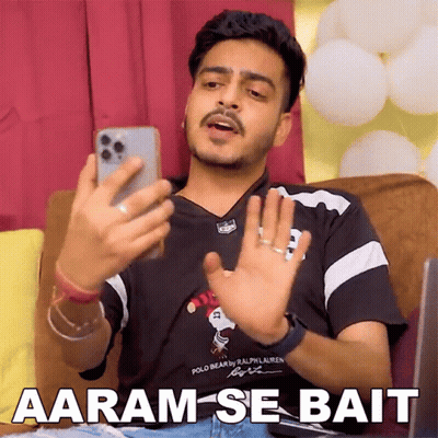 Man Sitting On Couch Looking At Phone Says Aaram-Se-Bait GIF