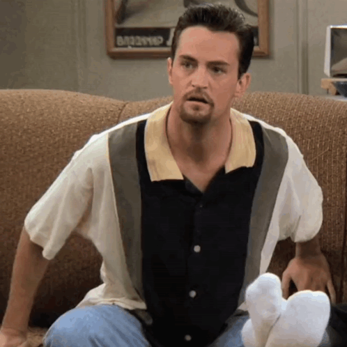 Man Sitting On Couch With Feet Up And Dancing Sign GIF