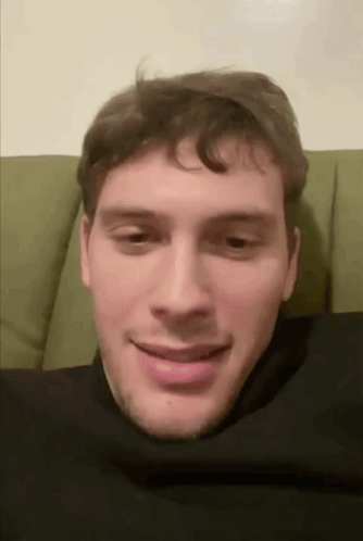 Man Sitting On Green Couch With Head In Black Turtleneck GIF