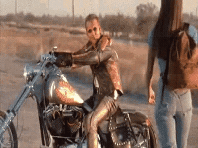 Man Sitting On Motorcycle In Desert, Woman Behind GIF