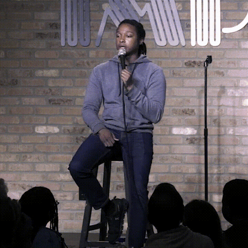 Man Sitting On Stool Speaking Into Microphone In Front Of Brick Wall GIF