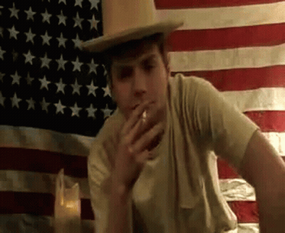 Man Smoking Cigarette In Front Of American Flag GIF
