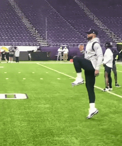 Man Squatting On Football Field In Front Of Stadium GIF