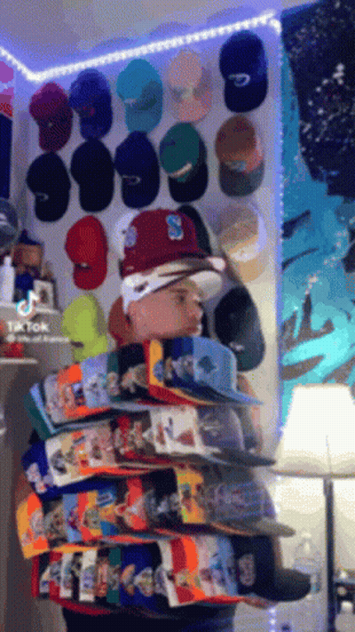 Man Standing Before Wall Of Hats With Letter S GIF
