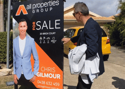 Man Standing In Front Of All Properties Group Sign GIF