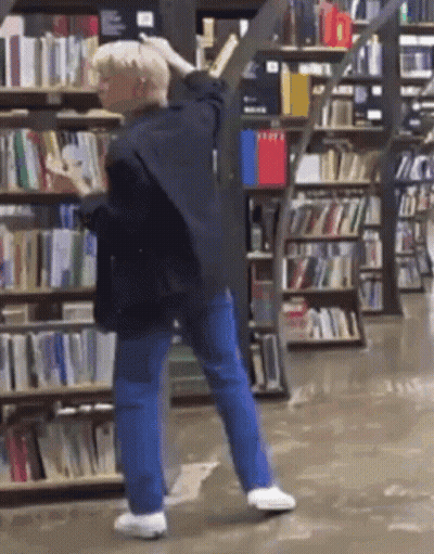Man Standing In Front Of Bookshelf In Bookstore GIF