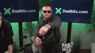 Man Standing In Front Of Duelbits Banner GIF