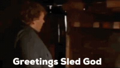 Man Standing In Front Of Fireplace Saying Greetings Sled God GIF