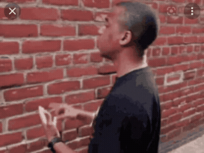 Man Standing In Front Of Red Brick Wall Holding Paper GIF