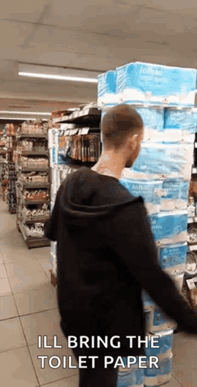Man Standing In Front Of Stacked Toilet Paper Rolls GIF