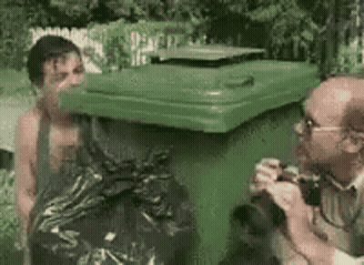 Man Standing Next To Green Trash Can While Another Takes Picture GIF