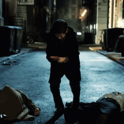 Man Standing Next To Man Laying On Ground In Dark Alleyway GIF