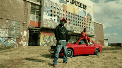 Man Standing Next To Red Car In Front Of Ethu Building GIF