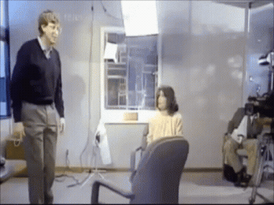 Man Standing Next To Woman In Chair GIF
