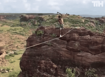 Man Standing On Rope On Rocky Cliff With Letters TH GIF