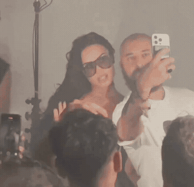 Man Taking Picture Of Woman In Sunglasses In Front Of Crowd GIF